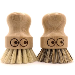 Op de afbeelding: Twee houten afwasborstels met natuurlijke borstels. De borstels hebben een afgeronde houten handvat met een schattig gezicht met twee ogen.