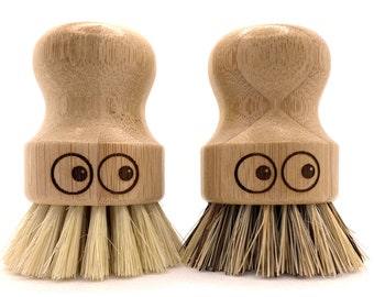 May include: Two wooden dish brushes with natural bristles. The brushes have a rounded wooden handle with a cute face with two eyes.