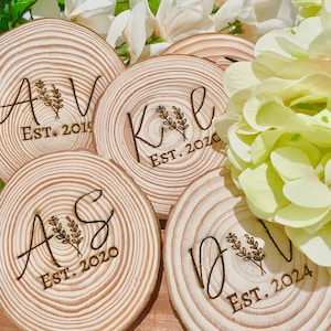 May include: Four wooden coasters with a natural wood finish. Each coaster features a different set of initials and the year established. The initials are A & V, K & E, A & S, and D & V. The years are 2019, 2020, 2020, and 2024.