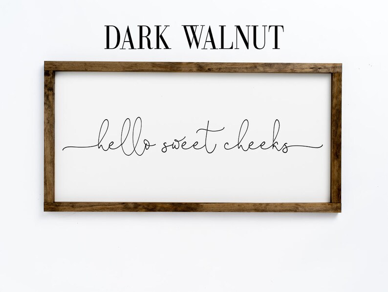 K&ouml;nnte beinhalten: Ein Holzschild mit einem dunkelbraunen Walnussrahmen und dem Text "hello sweet cheeks" in einer kursivschrift.