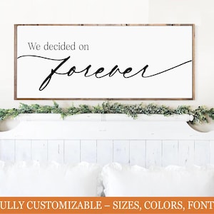 May include: A framed wooden sign with the words "We decided on Forever" in elegant black script. The sign hangs above a white headboard adorned with greenery and white pillows. The bottom of the image has text that says "FULLY CUSTOMIZABLE - SIZES, COLORS, FONTS".