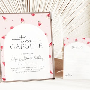 Może przedstawiać: Różowa i biała karta kapsuły czasu z ilustracjami arbuza. Na karcie napisano "Time Capsule" i "To be opened on Lily's Eighteenth Birthday". Mniejsza karta z tym samym wzorem arbuza zawiera napis "Dear Lily" i "with love."
