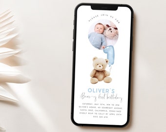 May include: A blue and white digital invitation for a baby's first birthday party. The invitation features a photo of a baby boy in a blue onesie holding a teddy bear. The invitation also features a teddy bear holding a blue balloon with the number one on it. The text on the invitation reads "Oliver's Bear-y First Birthday" and includes the date, time, location, and RSVP information.