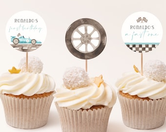May include: Three cupcakes decorated with racing car themed toppers. The toppers feature a blue race car, a tire, and a checkered flag with the text "Ronaldo's a fast one".