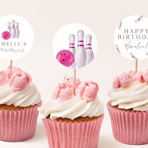 Peut inclure: Trois cupcakes roses et blancs avec un glaçage blanc et des pépites roses. Chaque cupcake est surmonté d'un rond de papier blanc avec une boule de bowling rose et des quilles blanches. Les toppers disent "Amelia's 8th birthday party", "Happy Birthday Amelia!" et "Happy Birthday Amelia!" avec des quilles roses en arrière-plan.
