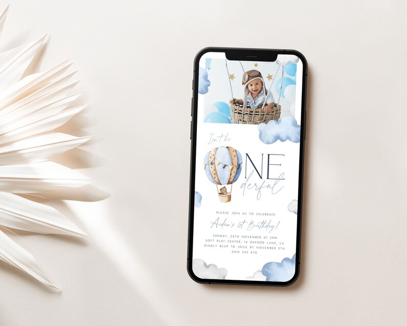 Op de afbeelding: Een digitale uitnodiging in blauw en wit met een aquarel-illustratie van een luchtballon en wolken. De tekst luidt "Isn't he one derful" en "Please join us to celebrate Aden's 1st Birthday!" met details over het evenement.