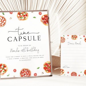 May include: A white sign with a black frame and the text "time capsule" in black cursive writing. The sign also includes the text "To be opened on Noah's 18th birthday" and instructions to write a special message for Noah. The sign is decorated with watercolour illustrations of pizza slices, tomatoes, mushrooms, and basil leaves.