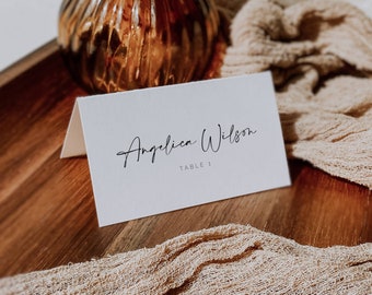 May include: White place card with black calligraphy that reads "Angelica Wilson" and "Table 1".