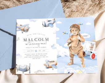 May include: A blue and white airplane themed first birthday party invitation with a photo of a baby boy wearing a brown aviator hat and overalls. The invitation includes the text "On my, how time flies. Malcolm is turning one! Please fly on over to celebrate. June 25th 1pm - 3pm. Malcolm's House, 26 Preston Avenue, Barstow, California, 95062-3422. Kindly RSVP to Katherine by June 10th. 0412 345 678."