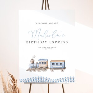 Peut inclure: Une pancarte d'accueil blanche avec du texte bleu qui dit "Bienvenue &agrave; bord de l'Express d'anniversaire de Malcolm. Prenez place et pr&eacute;parez-vous au d&eacute;part."  Une illustration aquarelle d'un train bleu et brun avec de la fum&eacute;e blanche se trouve sous le texte. Le train est sur une voie ferr&eacute;e &agrave; carreaux bleus et blancs.