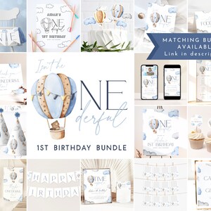 Op de afbeelding: Een blauwe en bruine luchtballon met een teddybeer in de mand. De ballon is omringd door wolken en de tekst "Isn't he one-derful" is geschreven in een blauw en wit lettertype. De tekst "1st Birthday Bundle" staat onder de ballon.