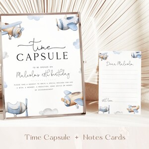 May include: A white sign with blue and brown airplanes and clouds. The sign says "Time Capsule" and "To be opened on Malcolm's 18th birthday".  Please take a moment to write a special message for him - a wish, a memory, a prediction, some advice or words of encouragement.  There are also several blank note cards with blue and brown airplanes and clouds. The note cards say "Dear Malcolm" and "with love".