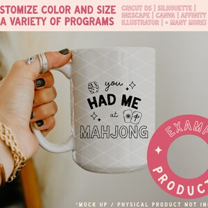 May include: White ceramic mug with the text "you had me at MAHJONG" in black. The mug has a diamond pattern and is held by a hand with rings and a bracelet. The mug also has the text "CUSTOMIZE COLOR AND SIZE IN A VARIETY OF PROGRAMS".