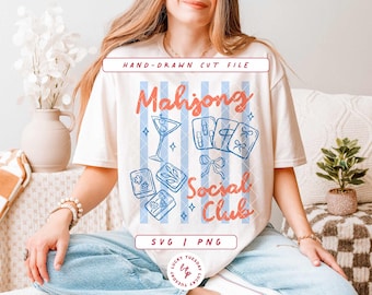 Może przedstawiać: Kremowy t-shirt z grafiką w jasnoniebieskie pionowe paski, niebieskimi rysunkami płytek mahjong, kieliszkiem do martini i kokardą. Napis Mahjong Social Club w kolorze pomarańczowym oraz etykiety Hand-Drawn Cut File i SVG | PNG.