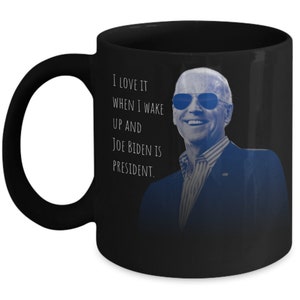 Peut inclure: Mug en céramique noire avec une image bleutée de Joe Biden portant des lunettes de soleil. Le mug porte le texte "I LOVE IT WHEN I WAKE UP AND JOE BIDEN IS PRESIDENT."