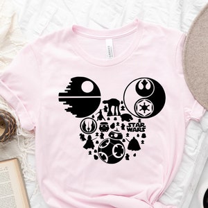 May include: A pink t-shirt with a black Mickey Mouse silhouette design featuring Star Wars characters and the text "Star Wars".