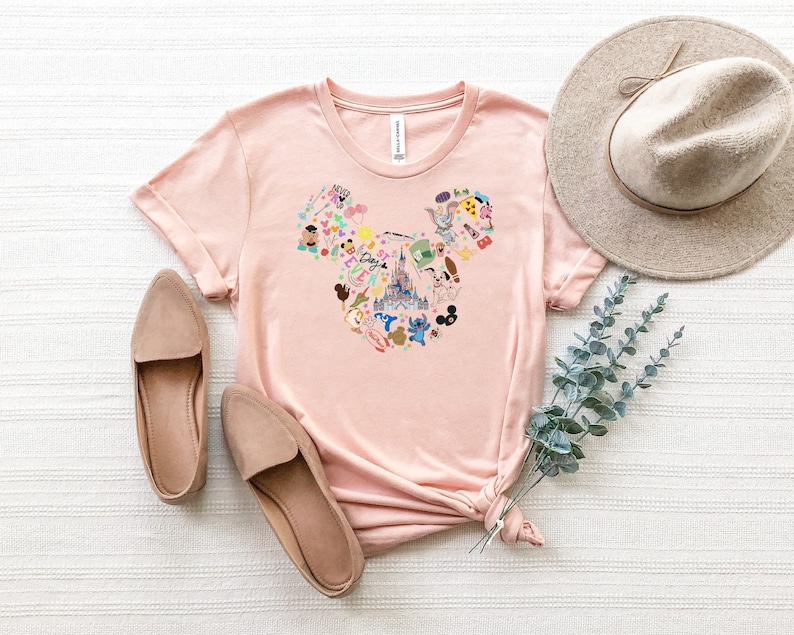 May include: A pink t-shirt with a graphic of a Mickey Mouse head made up of various Disney characters and icons. The graphic includes the Disney castle, Mickey Mouse, Minnie Mouse, Donald Duck, Goofy, Pluto, and other characters.