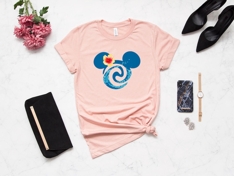 Puede incluir: Una camiseta rosa con un dise&ntilde;o de cabeza de Mickey Mouse azul y blanco con una flor en la parte superior. El dise&ntilde;o es un patr&oacute;n de onda estilizado.