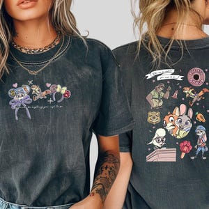 Pode incluir: T-shirt cinzenta escura com personagens de desenhos animados coloridos e o texto "You can be anything you wish to be." O design inclui um rato, uma raposa, um coelho e outras personagens. A parte de tr&aacute;s da camisa tem mais personagens de desenhos animados e o texto "The Big Donut."