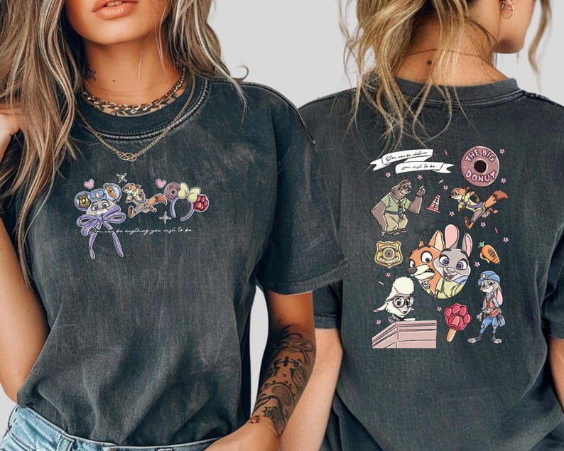 Pode incluir: T-shirt cinzenta escura com personagens de desenhos animados coloridos e o texto "You can be anything you wish to be." O design inclui um rato, uma raposa, um coelho e outras personagens. A parte de tr&aacute;s da camisa tem mais personagens de desenhos animados e o texto "The Big Donut."