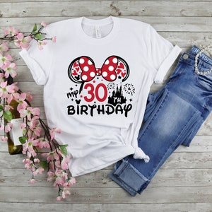 May include: White t-shirt with a black and red Minnie Mouse ears design. The shirt says "my 30 birthday" with a black castle and fireworks graphic.