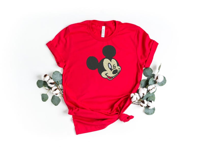 Puede incluir: Una camiseta roja con la cara sonriente de Mickey Mouse bordada en la parte delantera. El personaje cl&aacute;sico de dibujos animados aparece en la camiseta. La camiseta est&aacute; peinada con un nudo en la parte inferior y est&aacute; rodeada de vegetaci&oacute;n.