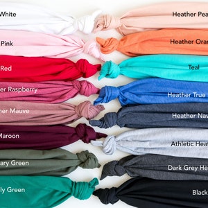 May include: A collection of fabric swatches in various colors, including white, pink, red, heather raspberry, heather mauve, maroon, military green, kelly green, heather peach, heather orange, teal, heather true royal, heather navy, athletic heather, dark grey heather, and black.