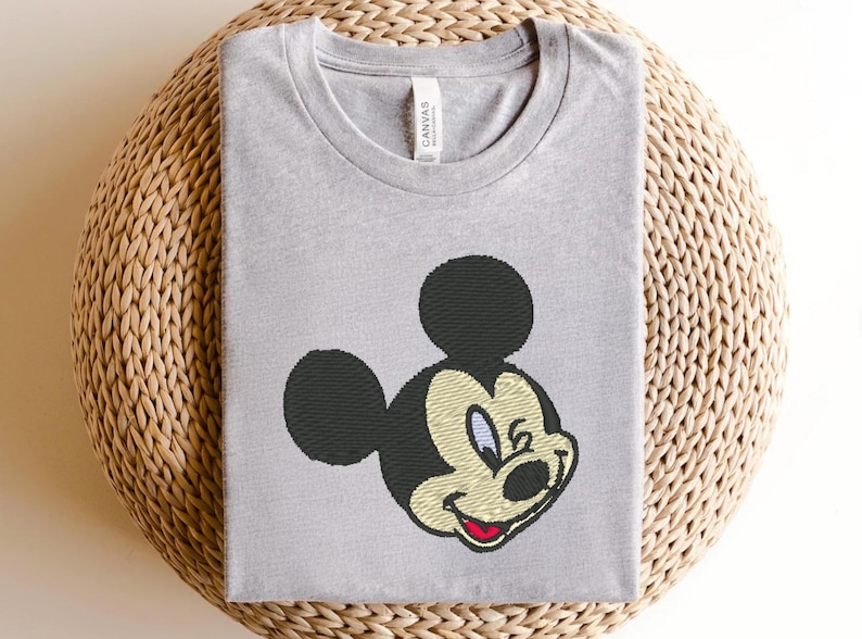 Puede incluir: Camiseta gris claro con un bordado de Mickey Mouse. El dise&ntilde;o incluye orejas negras, una cabeza negra y una cara sonriente con boca roja, hocico beige y ojos azules. La camiseta est&aacute; hecha de material suave.
