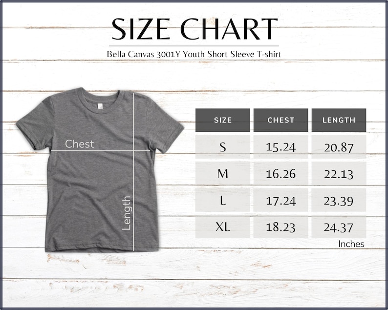 Pode incluir: Uma camiseta cinza de manga curta juvenil Bella Canvas 3001Y com uma tabela de tamanhos. A tabela mostra as medidas do peito e comprimento em polegadas para os tamanhos S, M, L e XL. A camiseta est&aacute; em um fundo de madeira branca.