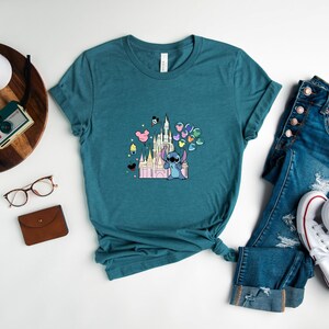 May include: Teal blue t-shirt with a graphic of Stitch holding balloons in front of Cinderella's Castle.