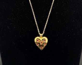 May include: A gold-tone necklace featuring a heart-shaped pendant. The pendant is decorated with a small, intricate butterfly motif in shades of red, orange, and black. The necklace hangs from a delicate gold-tone chain with a classic link design.