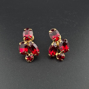 May include: A pair of vintage clip-on earrings. Each earring features a cluster of red, oval-cut rhinestones set in a gold-tone metal. The earrings have a classic, elegant design, perfect for formal occasions.