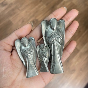May include: Three silver angel figurines carved from pyrite. The angels are in a praying position with their hands clasped together. The largest angel is about 2 inches tall.