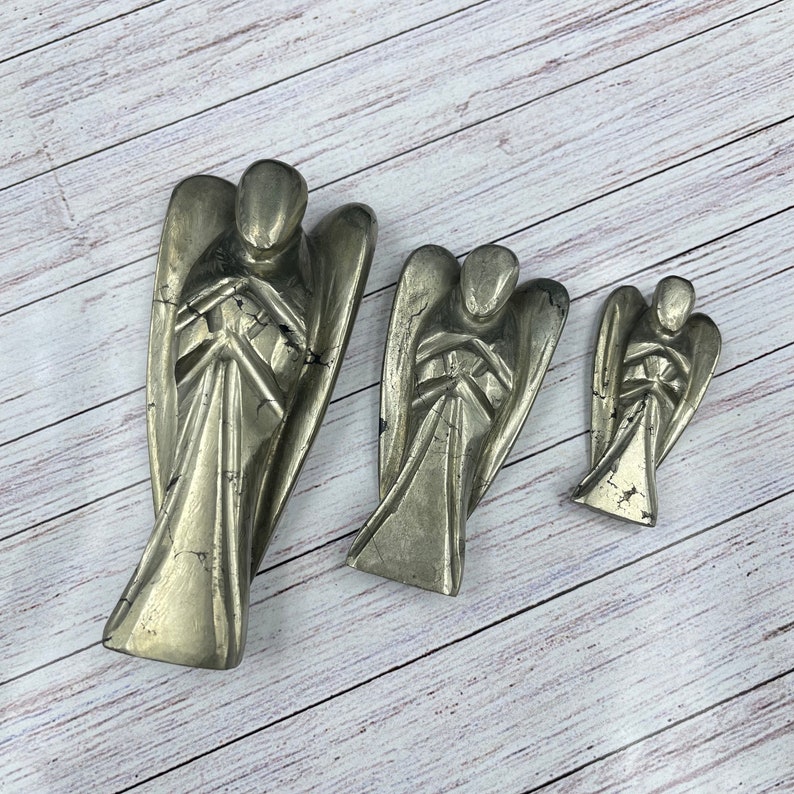 May include: Three pyrite angel figurines of varying sizes. The angels are carved from a metallic, gold-toned stone with a rough, textured surface.