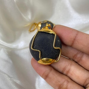 May include: A black stone pendant with a gold wire frame. The pendant is round and has a smooth surface.