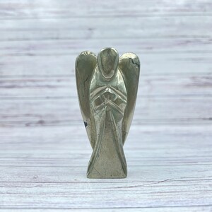 May include: A gold pyrite angel figurine with wings outstretched and hands clasped in prayer. The figurine is carved from a single piece of pyrite and has a natural, rough texture.