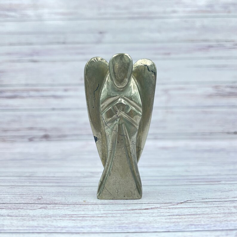 May include: A gold pyrite angel figurine with wings outstretched and hands clasped in prayer. The figurine is carved from a single piece of pyrite and has a natural, rough texture.