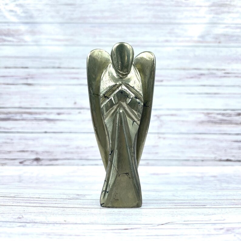 May include: A gold pyrite angel figurine with a detailed design. The angel is standing with its hands clasped in front of its chest.