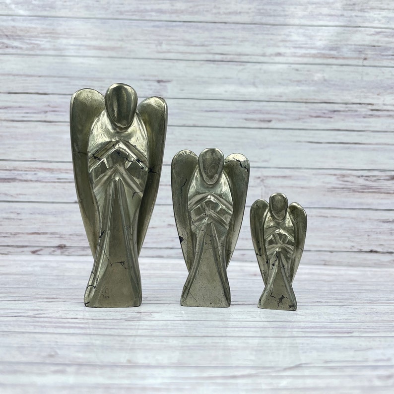 May include: Three gold pyrite angel figurines of varying sizes. The angels are carved from pyrite and have a metallic sheen. The largest angel is about 4 inches tall, the middle angel is about 3 inches tall, and the smallest angel is about 2 inches tall.