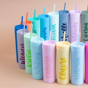 Puede incluir: Una colecci&oacute;n de vasos personalizados de colores con pajitas. Cada vaso es de un color diferente, incluyendo azul, rosa, verde y amarillo, y presenta un nombre en un color complementario. Los vasos est&aacute;n dispuestos en semic&iacute;rculo.