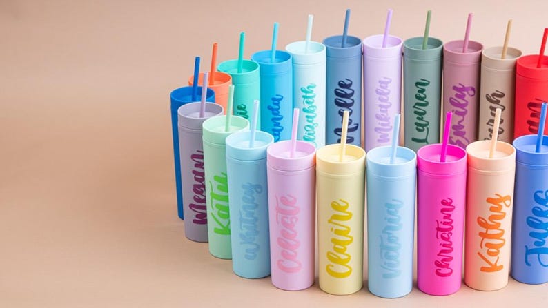 Puede incluir: Una colecci&oacute;n de vasos personalizados de colores con pajitas. Cada vaso es de un color diferente, incluyendo azul, rosa, verde y amarillo, y presenta un nombre en un color complementario. Los vasos est&aacute;n dispuestos en semic&iacute;rculo.