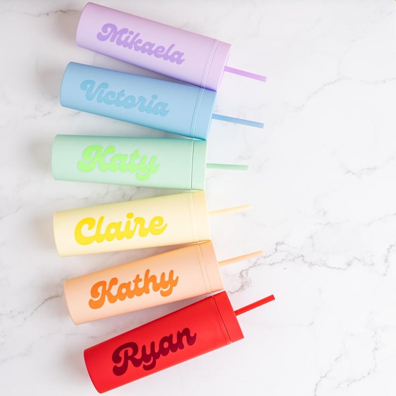 Puede incluir: Seis vasos de colores con pajitas, cada uno en un tono pastel diferente: lavanda, azul claro, verde menta, amarillo, melocot&oacute;n y rojo. Cada vaso est&aacute; personalizado con un nombre en una fuente retro coordinada. Los vasos est&aacute;n dispuestos sobre una superficie de m&aacute;rmol blanco.