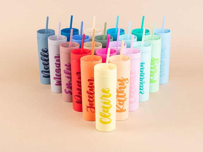 Puede incluir: Una colecci&oacute;n de vasos personalizados y coloridos con pajitas. Cada vaso es de un color diferente, incluyendo azul, rosa, naranja y verde, y presenta un nombre en una fuente de escritura a juego. Los vasos est&aacute;n dispuestos en forma triangular.