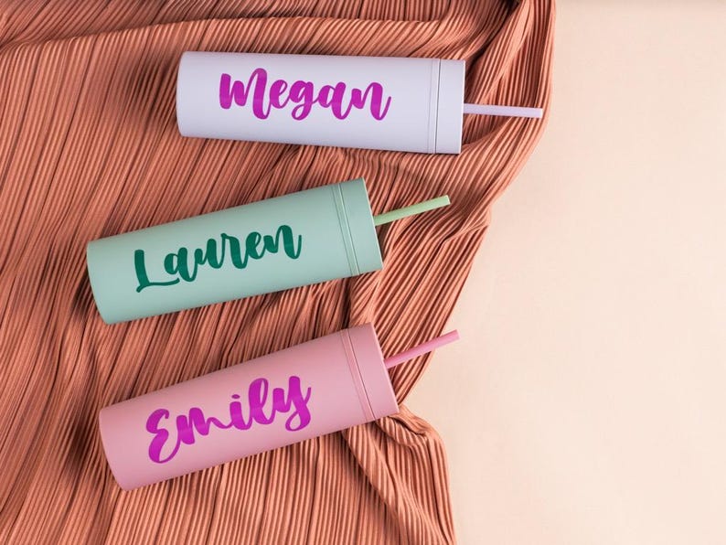 Puede incluir: Tres vasos personalizados en colores pastel: gris claro, verde menta y rosa. Cada vaso tiene un nombre en un color contrastante: "Megan", "Lauren" y "Emily". Los vasos tienen pajitas a juego y est&aacute;n sobre una tela plisada color melocot&oacute;n.