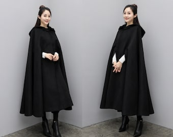 May include: Two women wearing black hooded capes with long sleeves. The capes are knee-length and have a simple design.