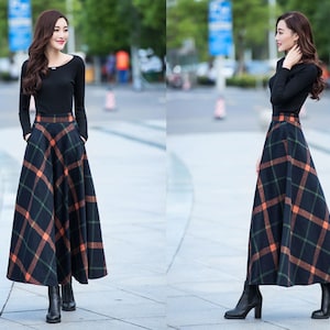 Peut inclure: Une femme porte une chemise noire &agrave; manches longues et une longue jupe &agrave; carreaux noirs et orange. Elle porte des bottes &agrave; talons noires.