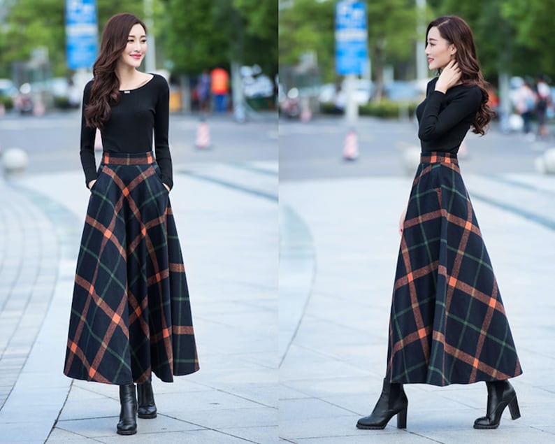 Peut inclure: Une femme porte une chemise noire &agrave; manches longues et une longue jupe &agrave; carreaux noirs et orange. Elle porte des bottes &agrave; talons noires.