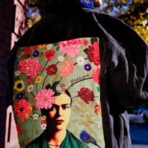 May include: Dark denim jacket with a Frida Kahlo-inspired design on the back. The artwork features vibrant pink, red, and yellow flowers, a portrait of Frida, and the word "passion".