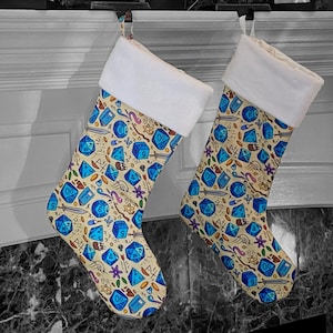May include: Two white Christmas stockings with a cream-colored cuff. The stockings are decorated with a pattern of blue dice and other gaming symbols on a beige background.