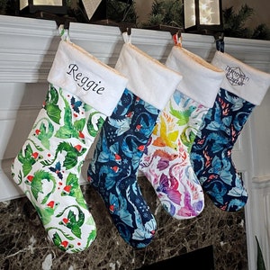 Puede incluir: Cuatro calcetines de Navidad personalizados con un diseño de dragón. Los calcetines son blancos con un puño esponjoso y presentan dragones de diferentes colores. Los nombres "Reggie" y "Dragon Slayer" están bordados en dos de los calcetines.